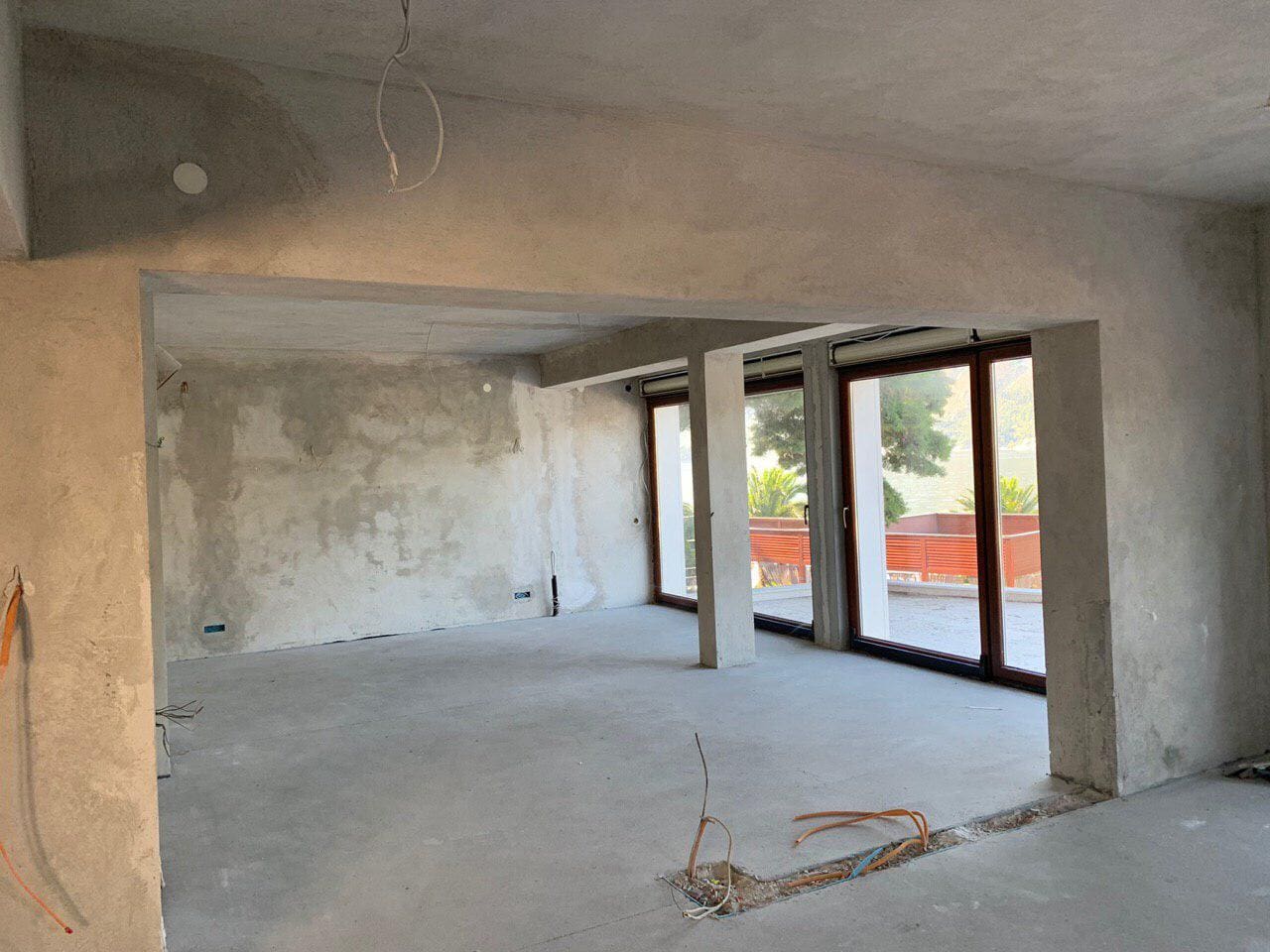 Unfinished living room in a villa under construction in Dobrota, Montenegro, with panoramic windows and access to the terrace.
