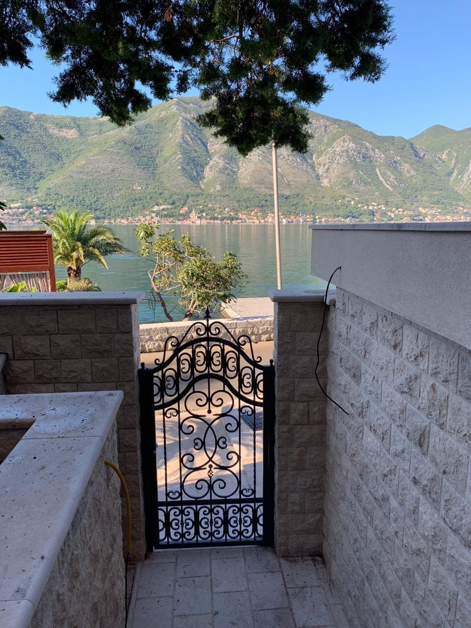 Wrought-iron gate and view of Kotor Bay from the villa terrace in Dobrota, Montenegro. Stone finishes and seascape.