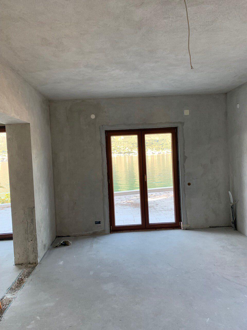 Living room under renovation in a villa in Dobrota, Montenegro, with a panoramic sea view through the balcony door.