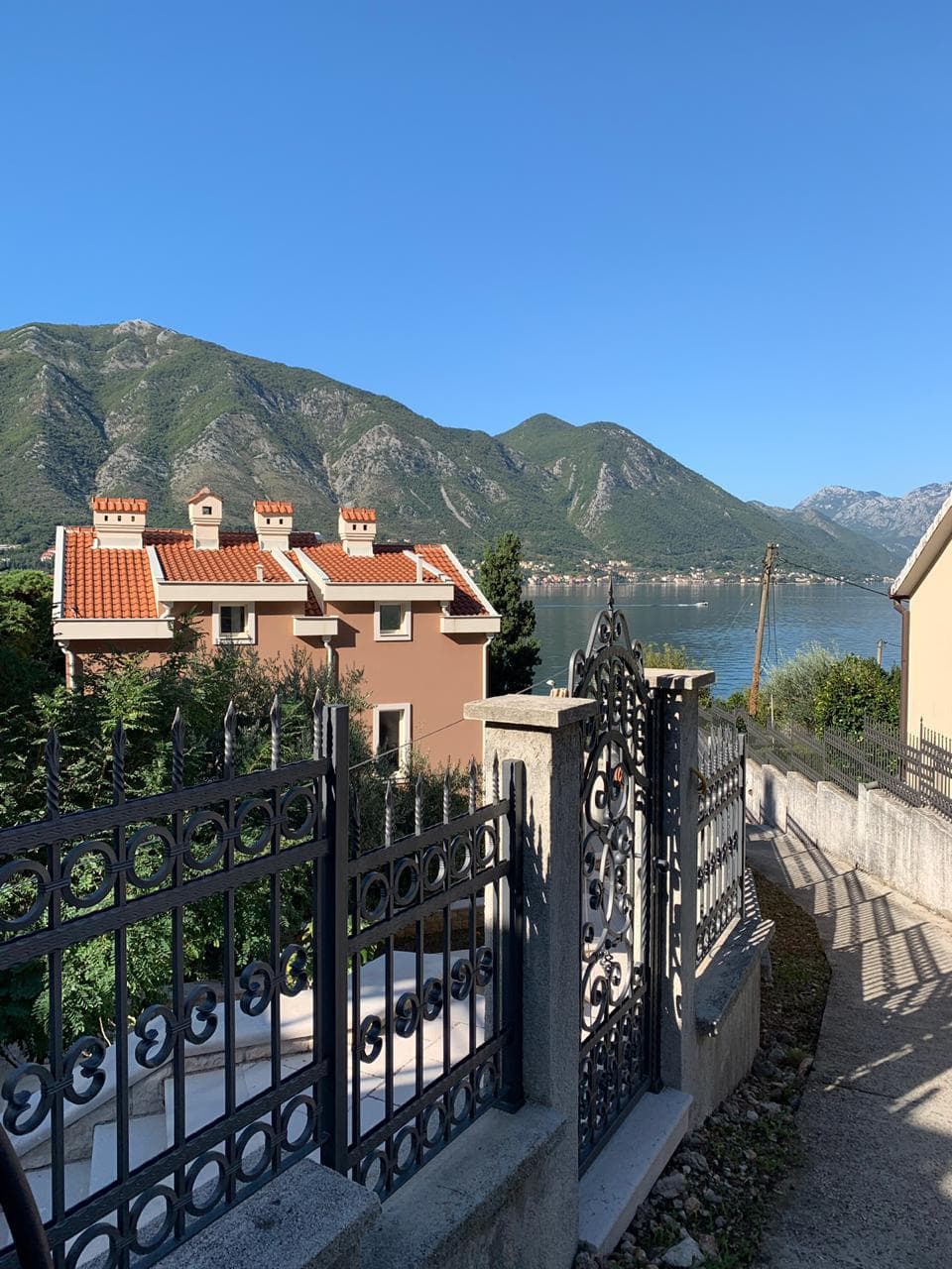 View of a villa with a wrought-iron fence and panoramic views of the Bay of Kotor and the mountains, Dobrota, Montenegro.