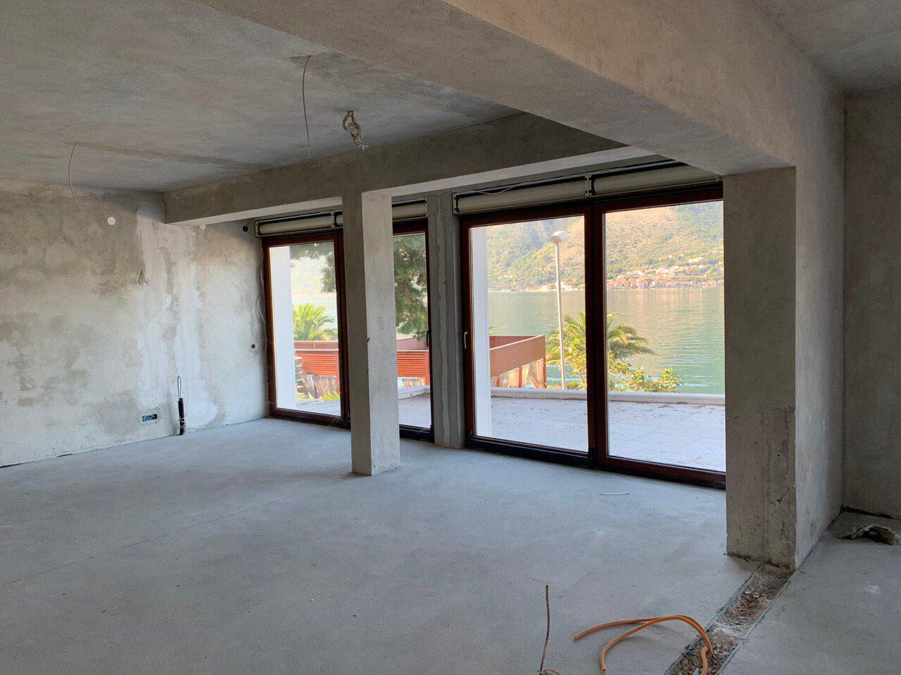 Unfinished living room in a villa under construction in Dobrota, Montenegro, with panoramic sea and mountain views through the terrace.