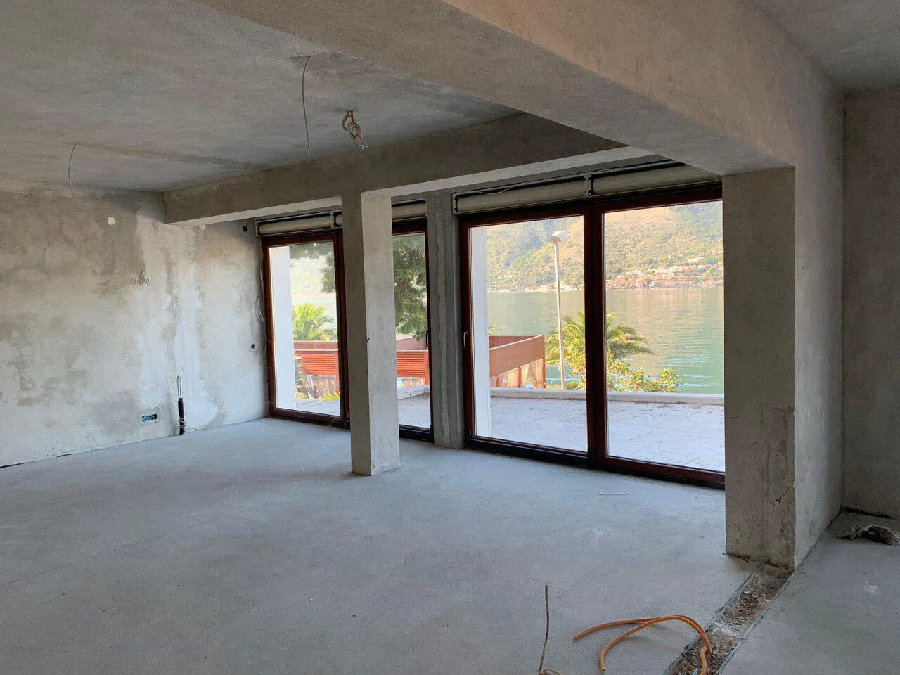 Unfinished room with concrete walls and large windows overlooking water. Prepared for finishing.