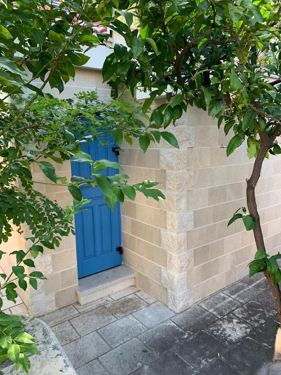 Blue villa door in Dobrota, Montenegro: stone facade finish, terrace, and a green tree in the property garden.