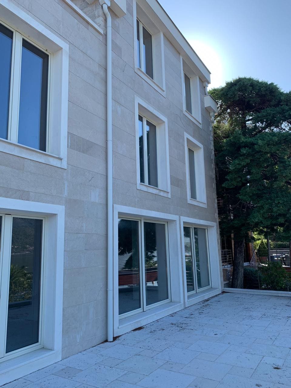 Facade of a modern villa made of light stone with panoramic windows in Dobrota, Montenegro.