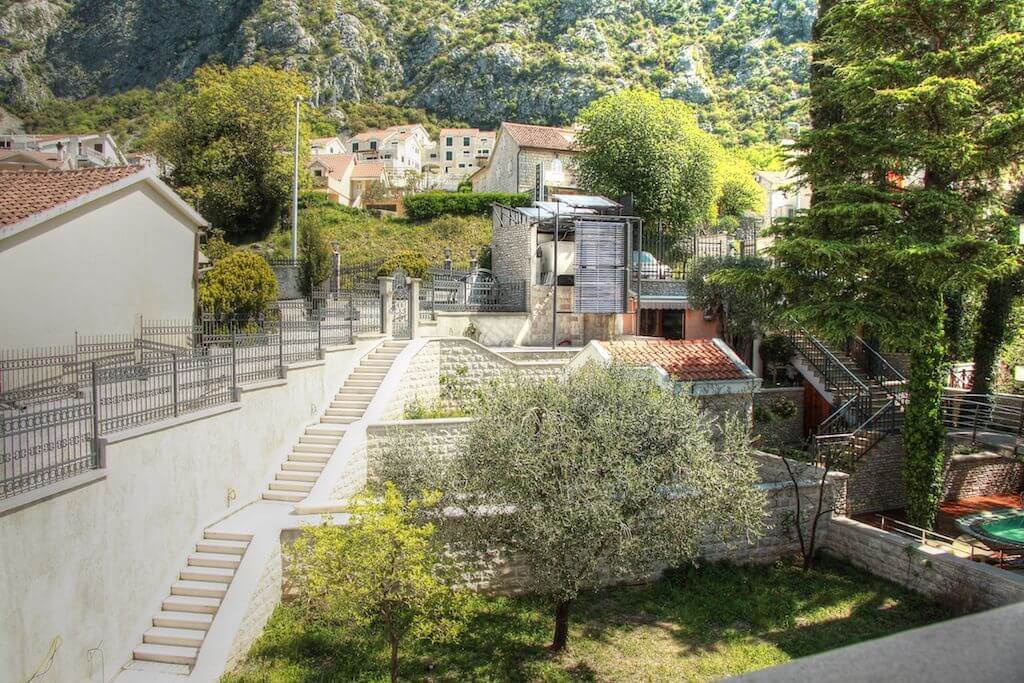 Villa grounds in Dobrota, Montenegro: stone stairs, a green garden with an olive tree, and mountain views.