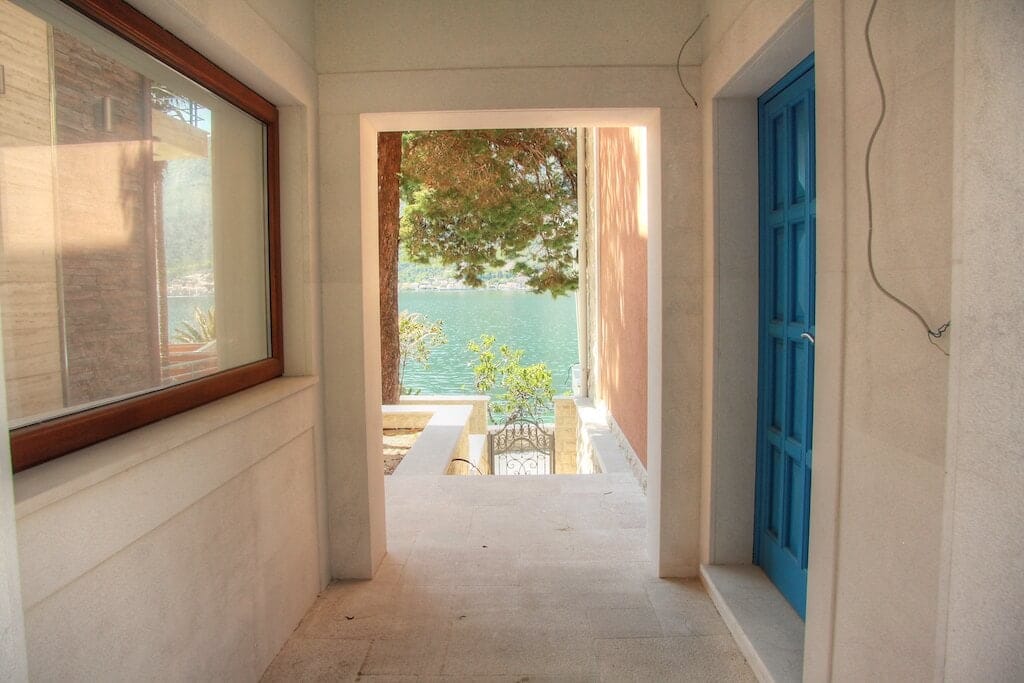 Sea view from the villa corridor in Dobrota, Montenegro: stone finishes, a blue door, and access to the coast.