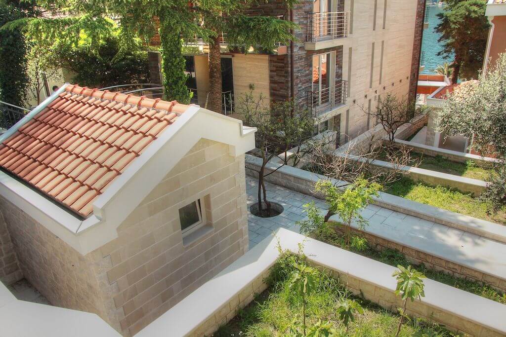 View of a stone villa with a tiled roof and a landscaped garden in Dobrota, Montenegro, overlooking the sea.