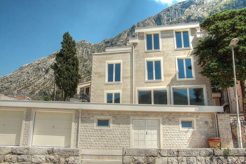 Exterior facade of a multi-story stone house with garage doors set against a mountain backdrop.