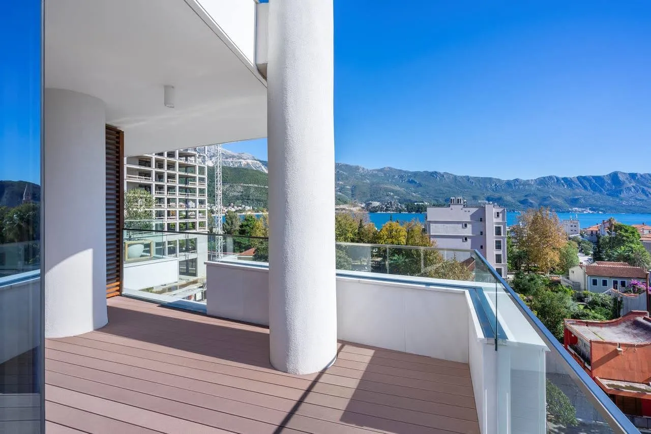 Balcony with wooden decking and glass railings overlooking the sea and mountains.