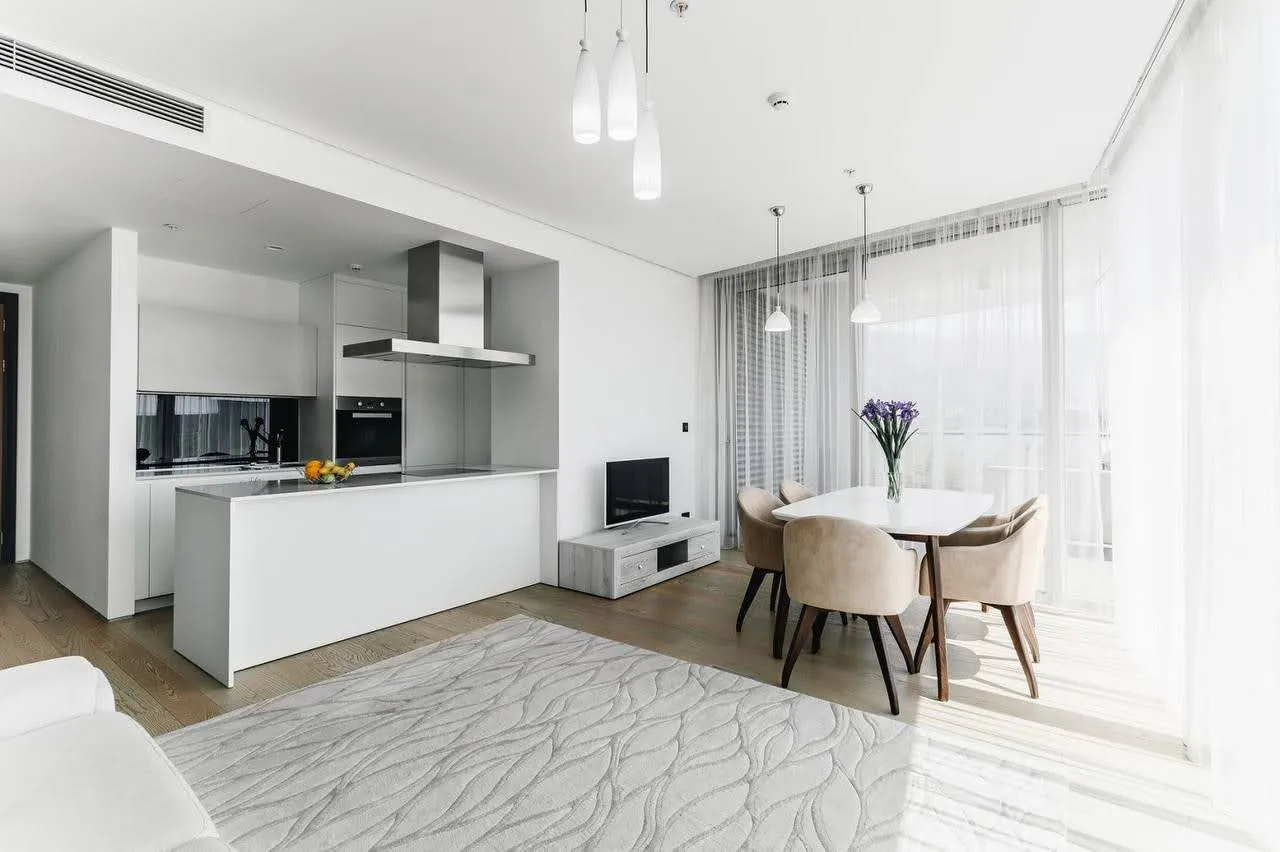 Modern open-plan living room with kitchen island, dining table, and sofa on a textured rug.