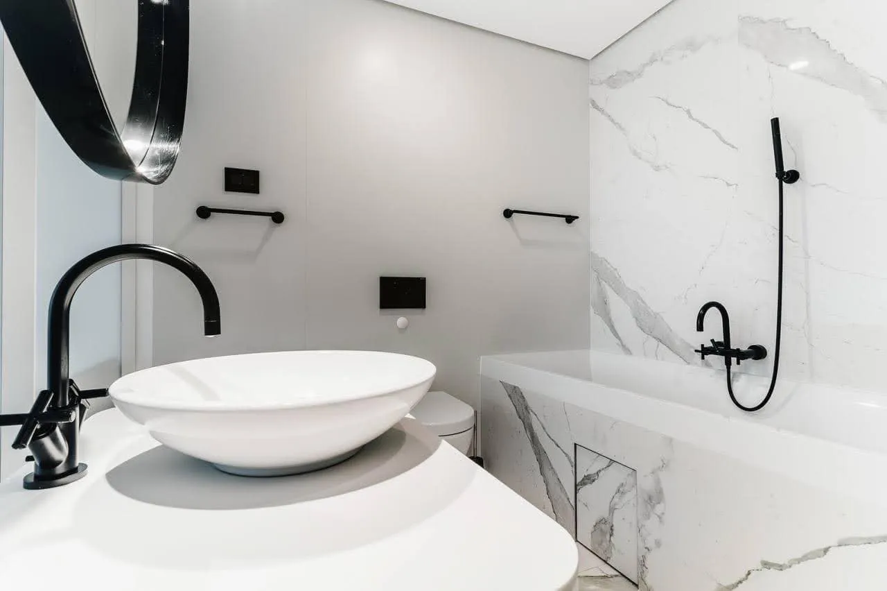 Modern bathroom featuring white marble, black fixtures, a round vessel sink, and a built-in bathtub.