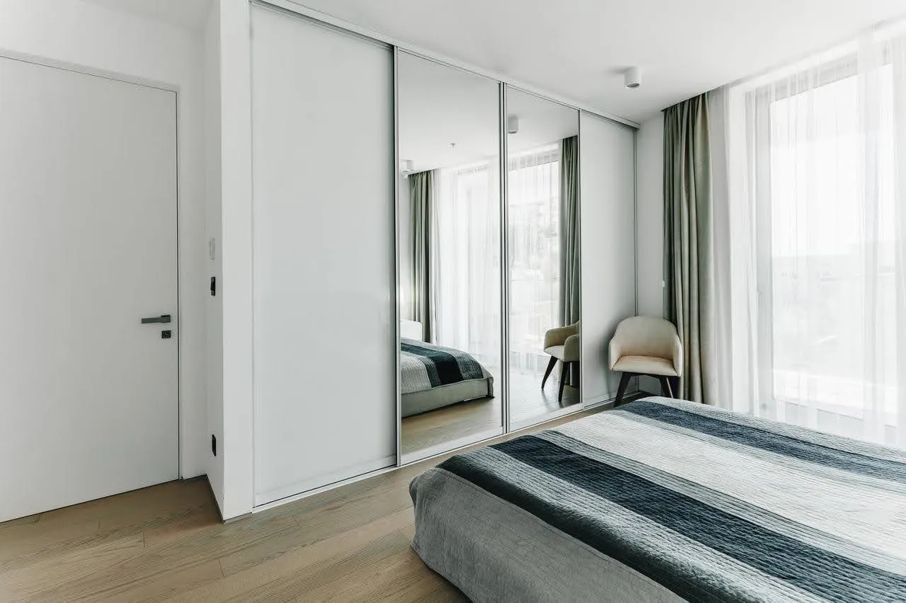 Modern bedroom featuring a double bed with striped bedding and a large built-in wardrobe with sliding mirrored doors.