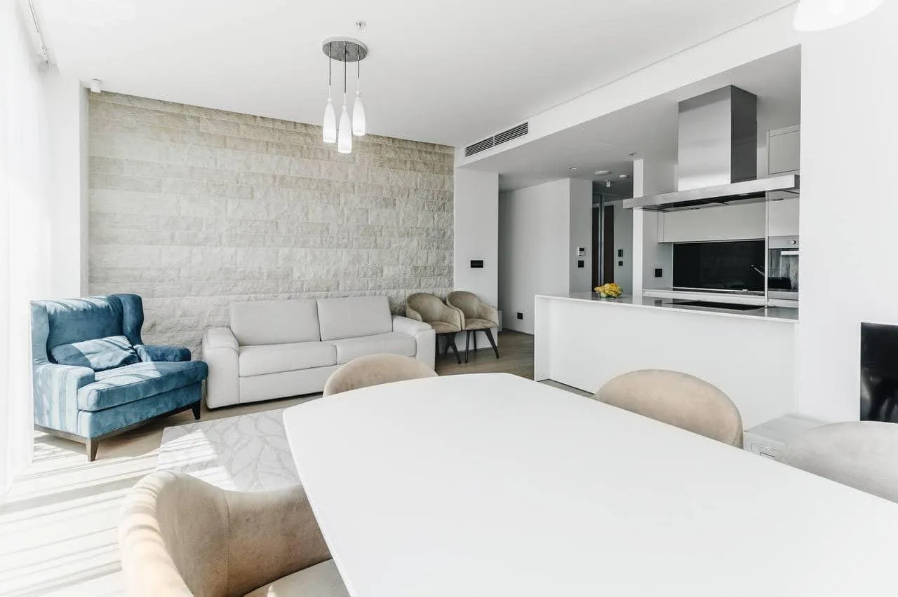 Modern living room with a sofa, blue armchair, dining table, and visible open kitchen area.