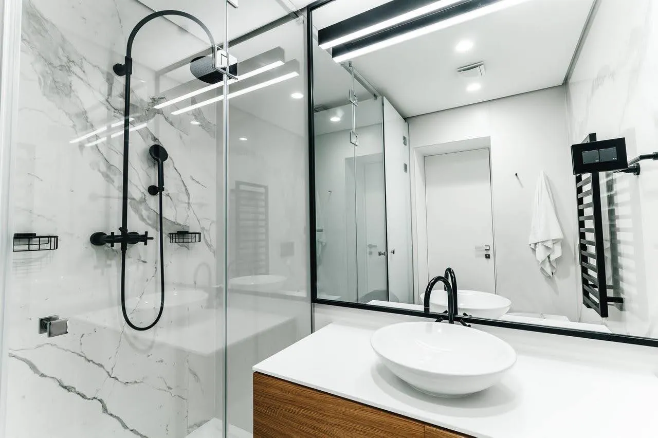 Modern bathroom with marble shower, black fixtures, and round vessel sink on a wooden vanity.