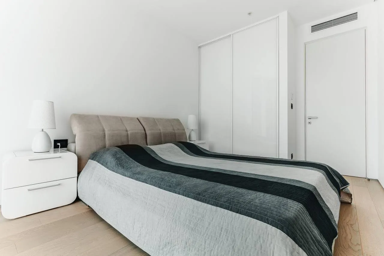 Modern bedroom featuring a double bed with striped bedding, white nightstands, and built-in wardrobe.