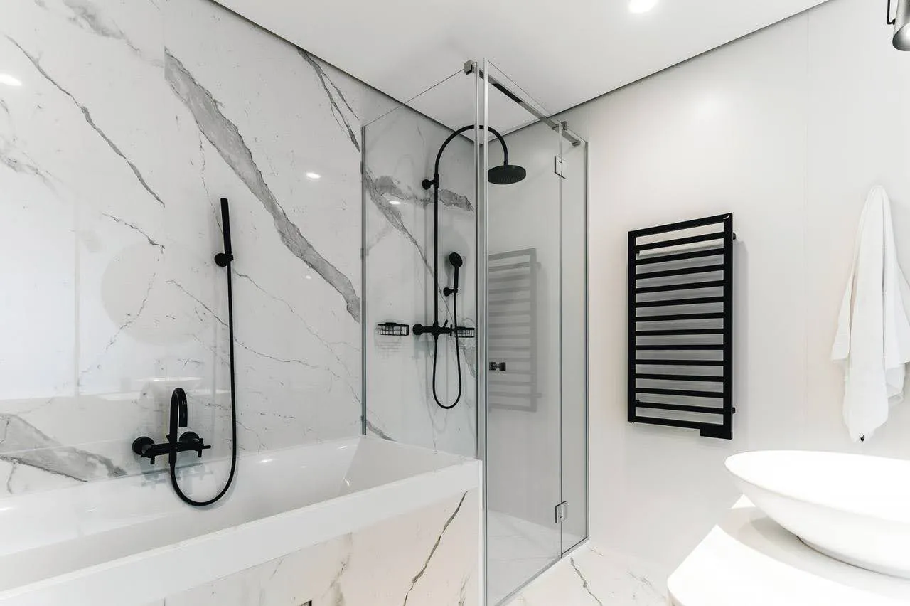 Modern bathroom with marble tiles, black fixtures, glass shower enclosure, and a heated towel rail.