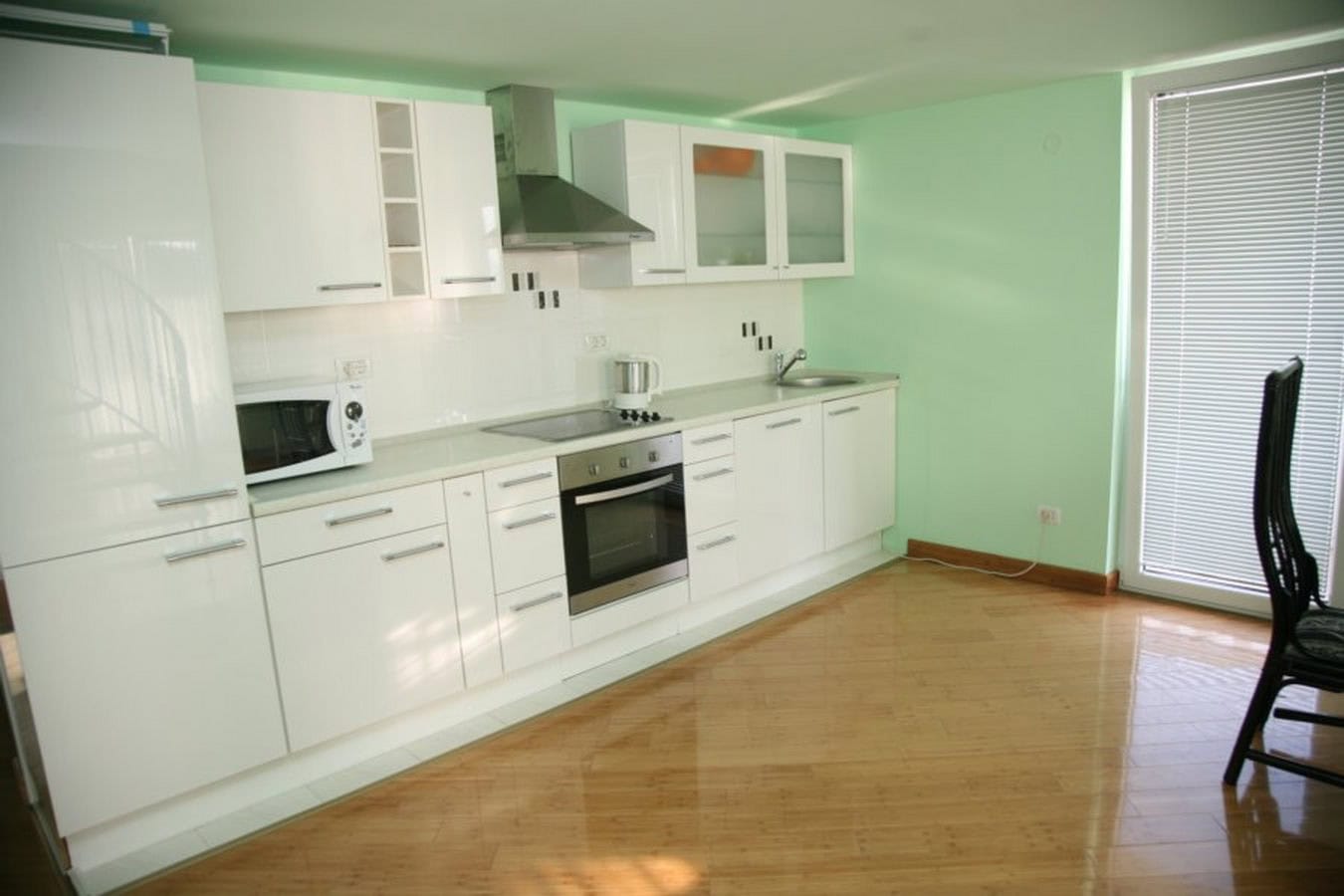 Modern white kitchen with appliances in a villa in Tivat, Montenegro: glossy cabinets, light walls, and parquet flooring.