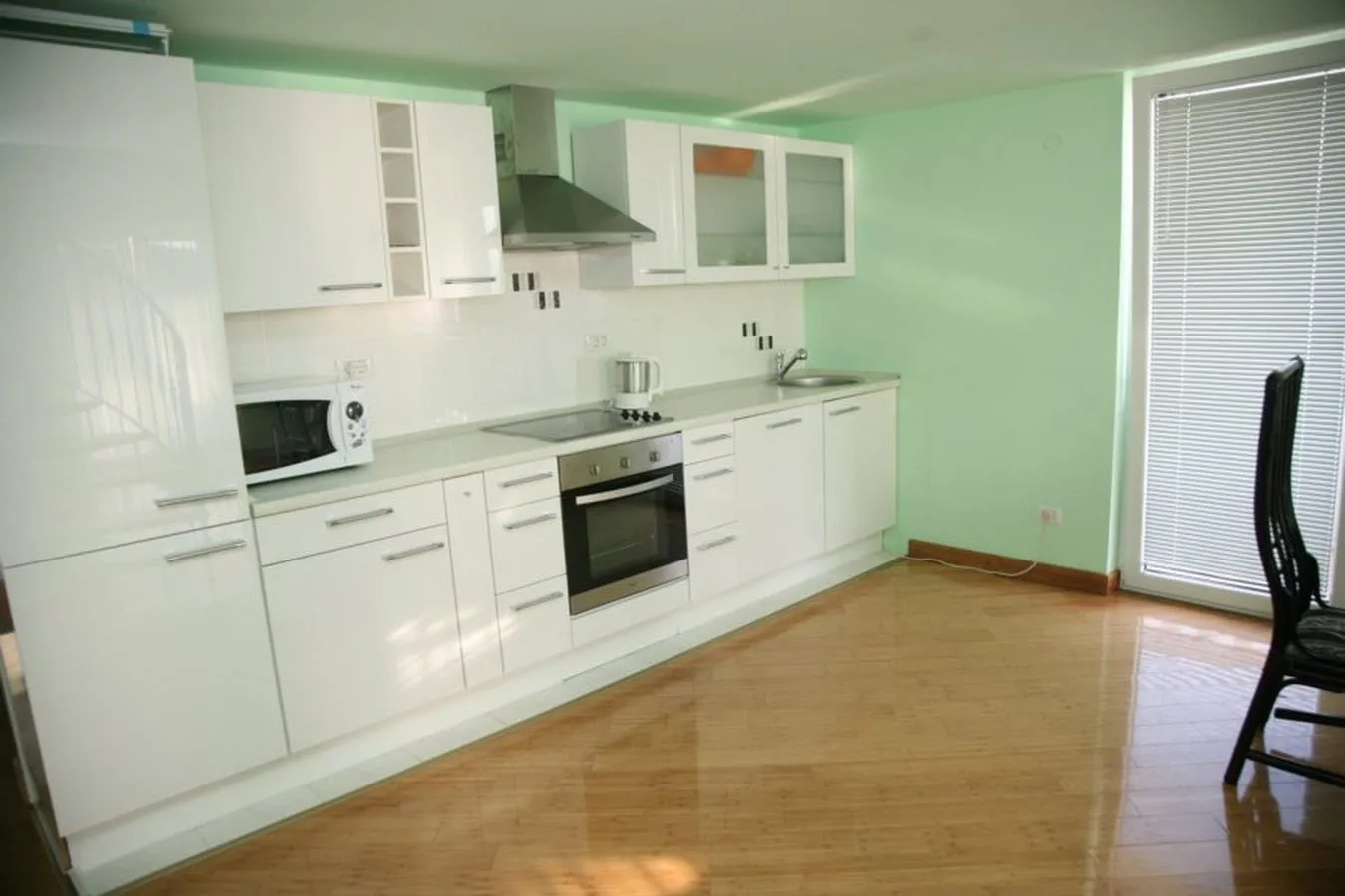 Modern kitchen featuring white glossy cabinets, built-in oven, hood, and light green walls.