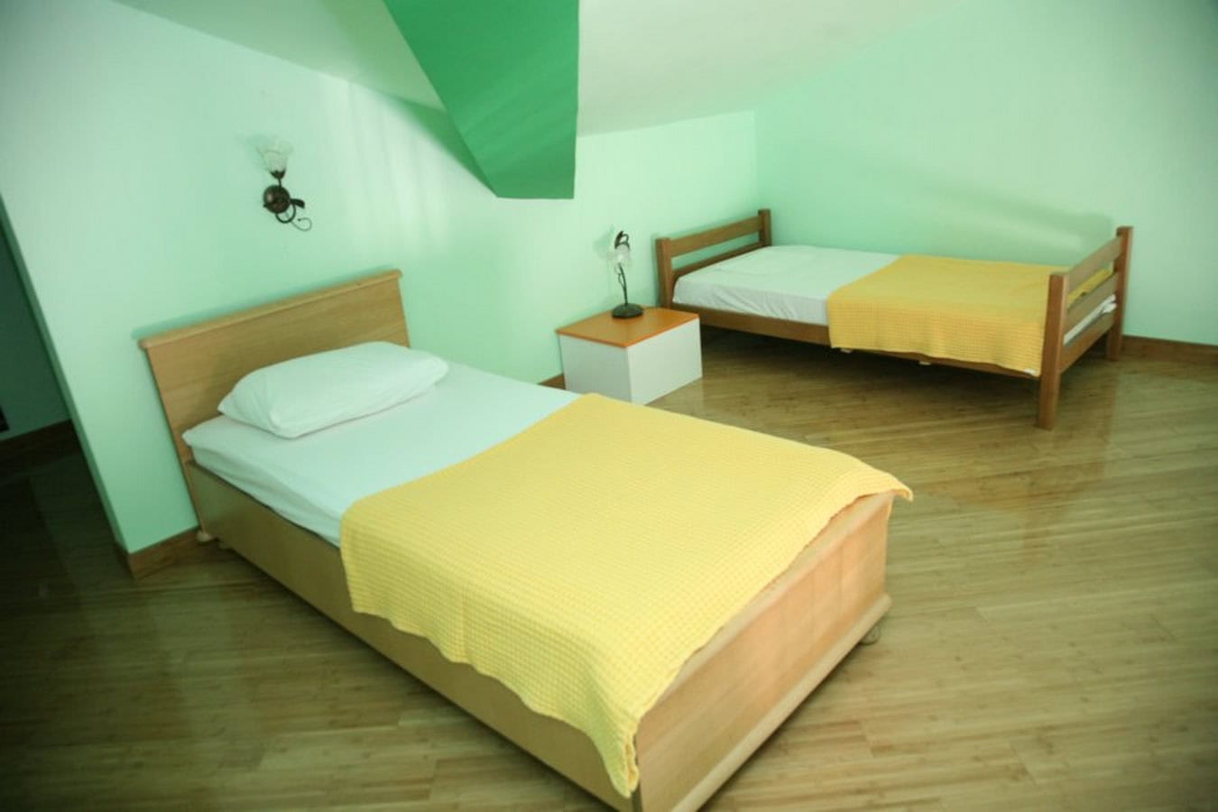 Bedroom with two beds in the attic of a villa in Tivat, Montenegro: light walls, wooden furniture and flooring.