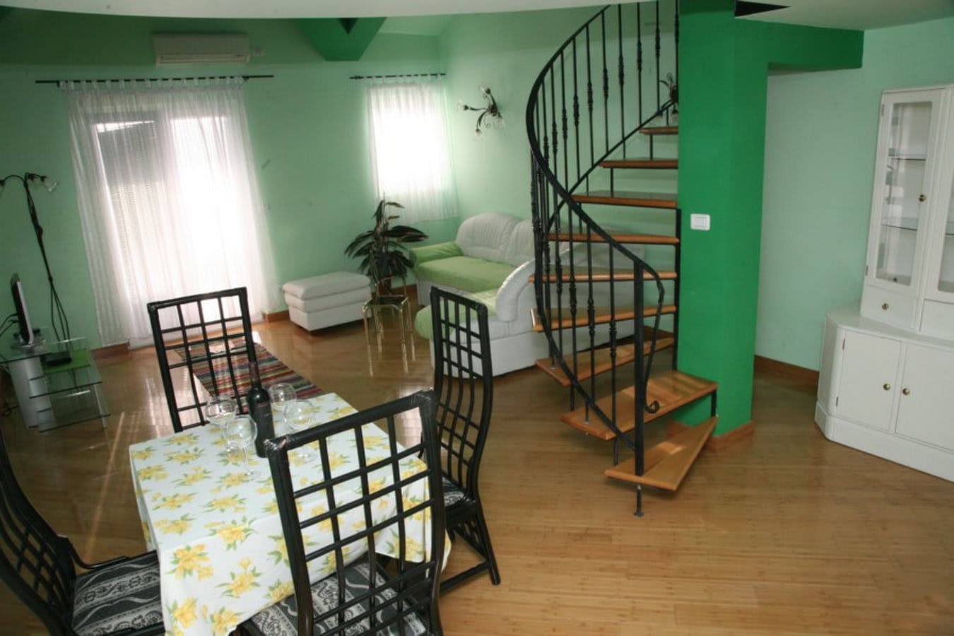 Living room with a spiral staircase and dining area in a villa in Tivat, Montenegro: bright interior, wooden floor.