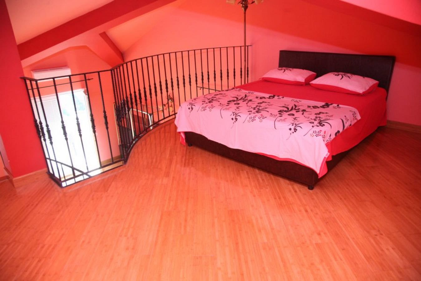 Bedroom in the attic of a villa in Tivat, Montenegro: double bed, wooden floor, and wrought-iron railing.