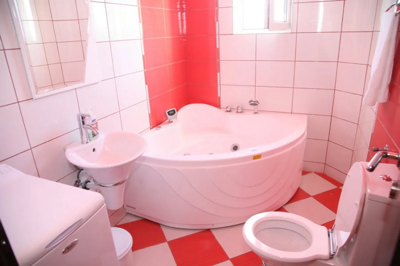 Bathroom featuring a corner bathtub, sink, and toilet in a red and white color scheme.