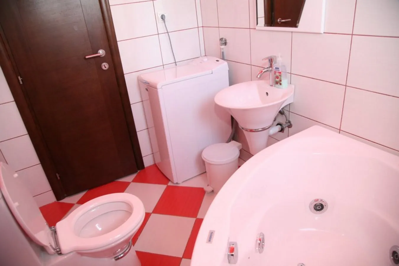 Bathroom featuring a white bathtub, sink, toilet, and washing machine on a red and white checkered floor.