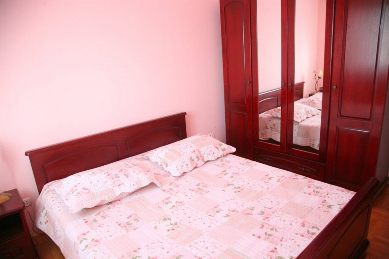 Bedroom in a villa in Tivat, Montenegro: a double bed and a dark wood wardrobe, pink walls, cozy interior.