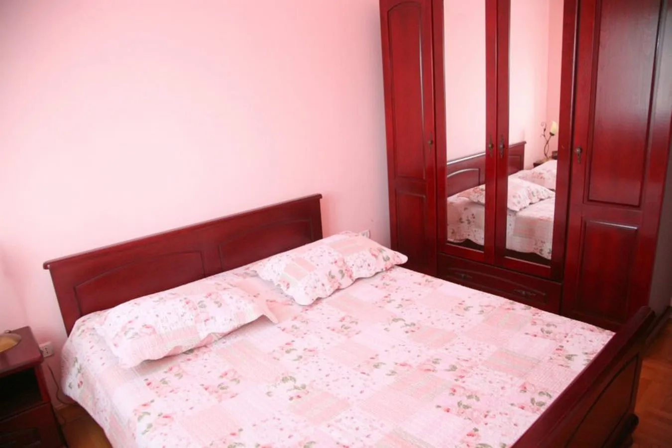 Bedroom featuring a wooden bed with floral bedding and a large mirrored wardrobe against pink walls.