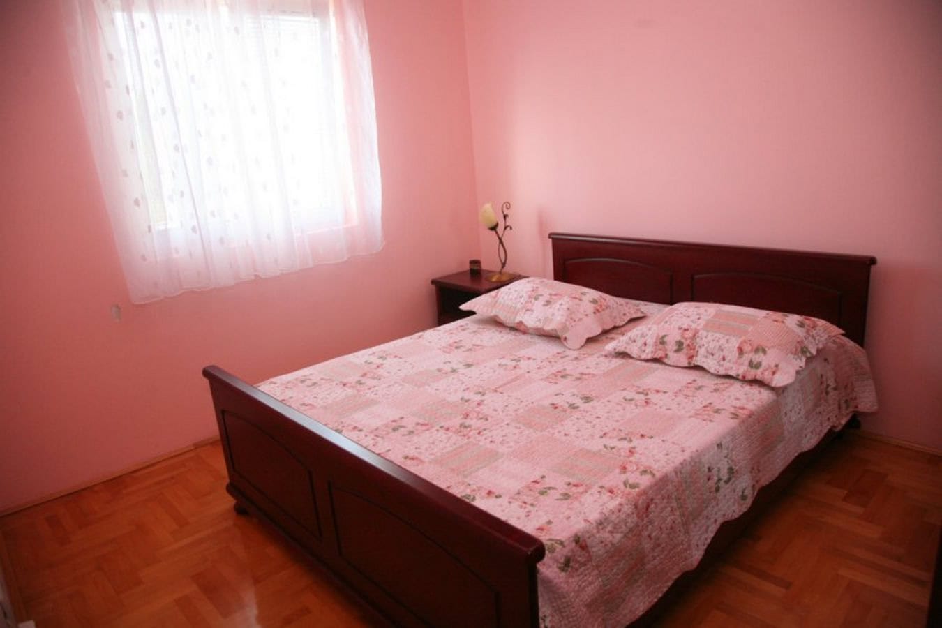 Bedroom with a double bed and parquet flooring in a villa in Tivat, Montenegro. Cozy interior in pink tones.