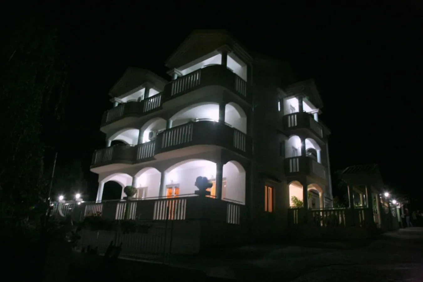 Night photo of a multi-story building with illuminated balconies and arched facade elements.