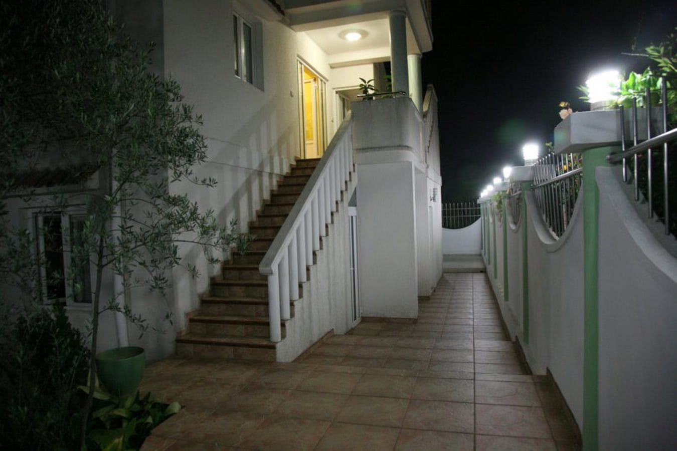 Evening view of the villa facade in Tivat, Montenegro: exterior staircase, lit terrace, and landscaped grounds.