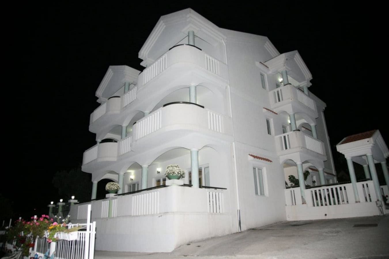 Three-story white villa in Tivat, Montenegro, with open balconies and nighttime facade lighting.