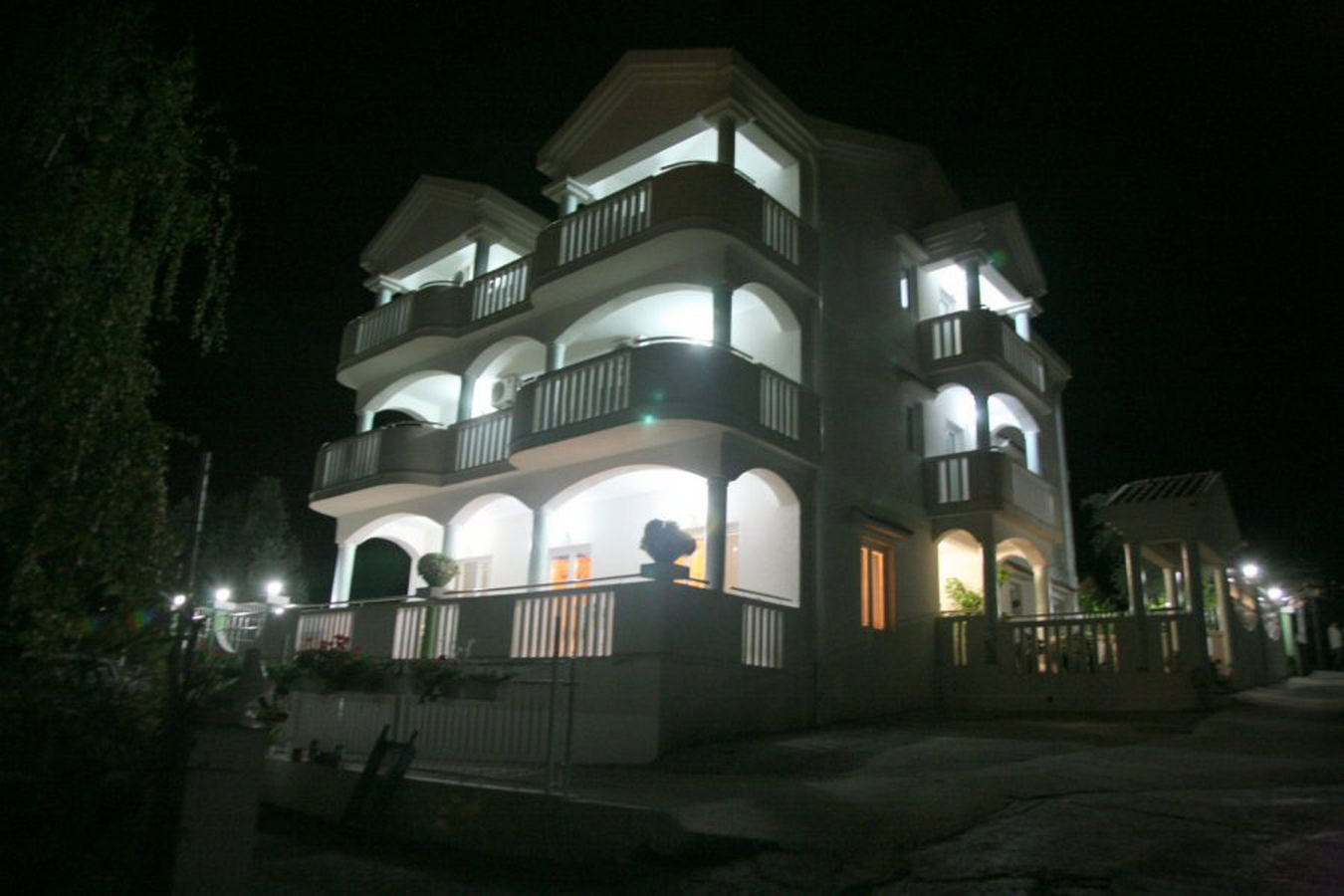 Three-story villa in Tivat, Montenegro, with illuminated terraces and balconies at night.