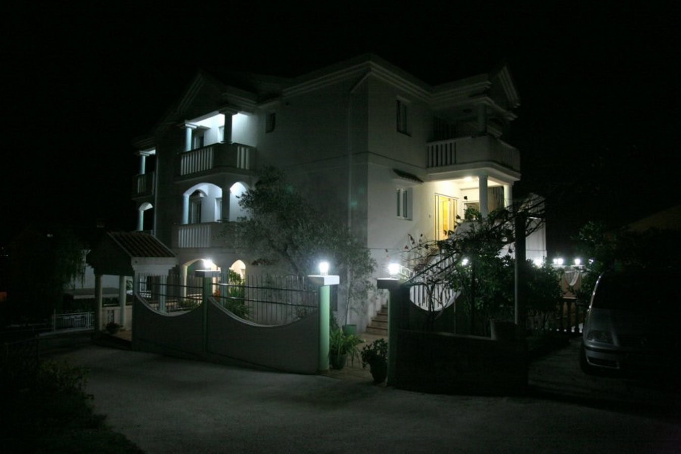 Three-story villa in Tivat, Montenegro, with night lighting, terraces, and a fenced yard.
