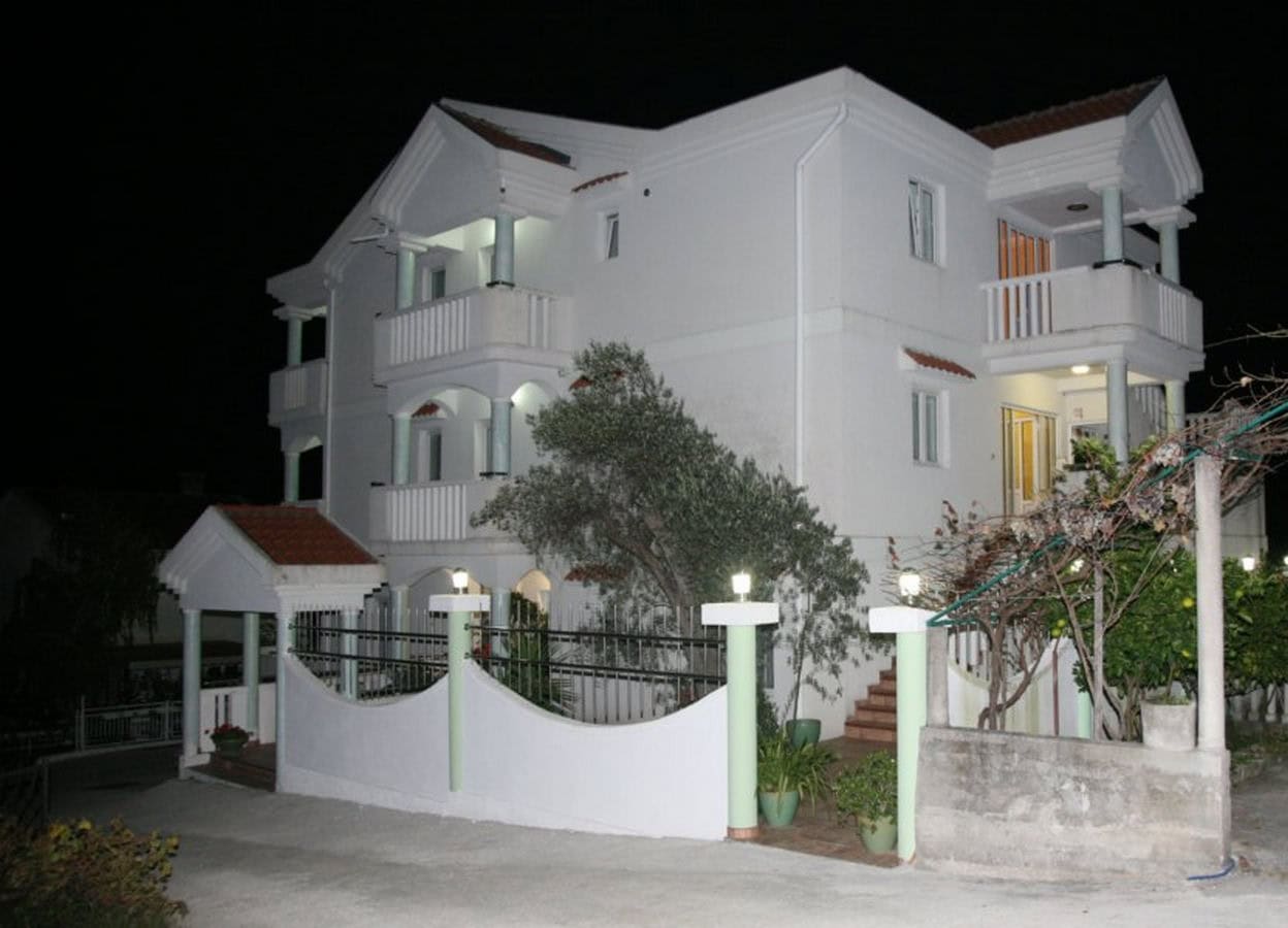 Three-story villa with balconies and a terrace in Tivat, Montenegro: night view of the illuminated facade and garden.