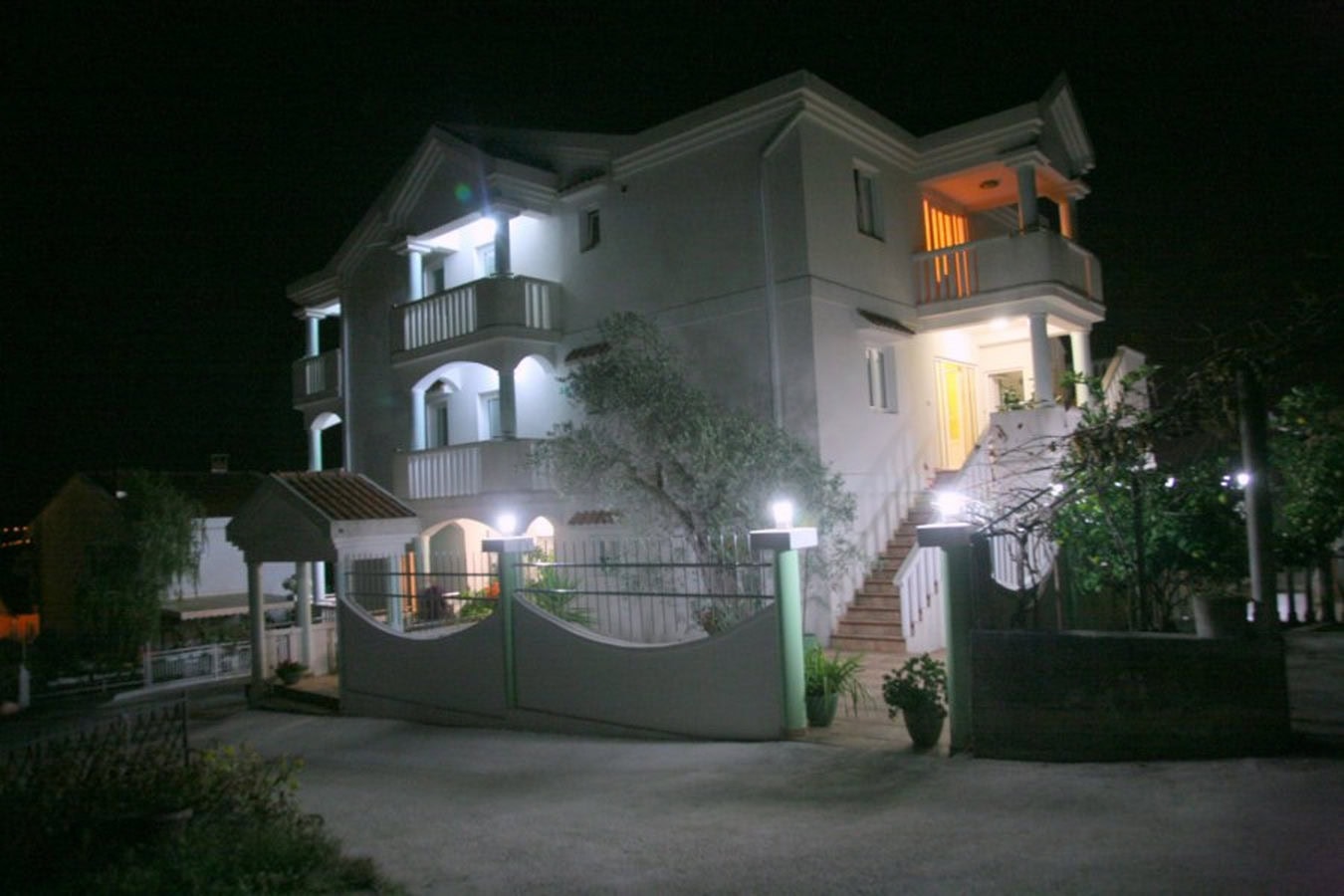 Three-story villa in Tivat, Montenegro: illuminated facade with balconies and staircase at night.