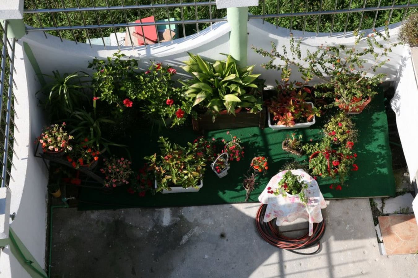 Cozy balcony with flowers and green flooring on a villa in Tivat, Montenegro: top view of the terrace with plants.
