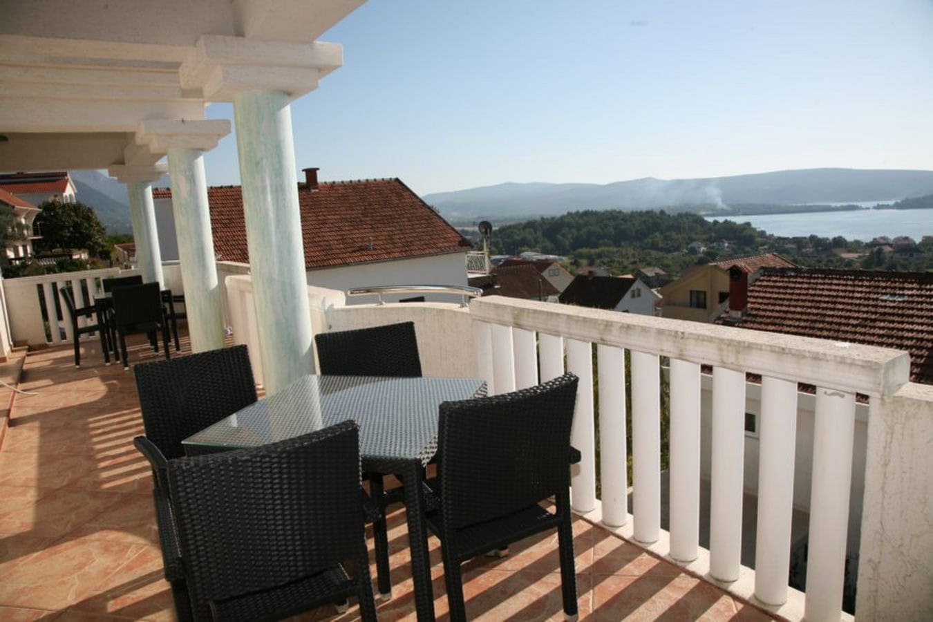 Villa terrace in Tivat, Montenegro: wicker chairs, a glass table, and panoramic sea and mountain views.