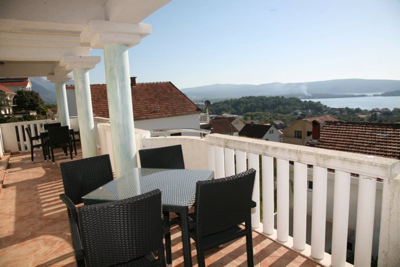 Villa terrace in Tivat, Montenegro: wicker chairs, a glass table, and panoramic sea and mountain views.