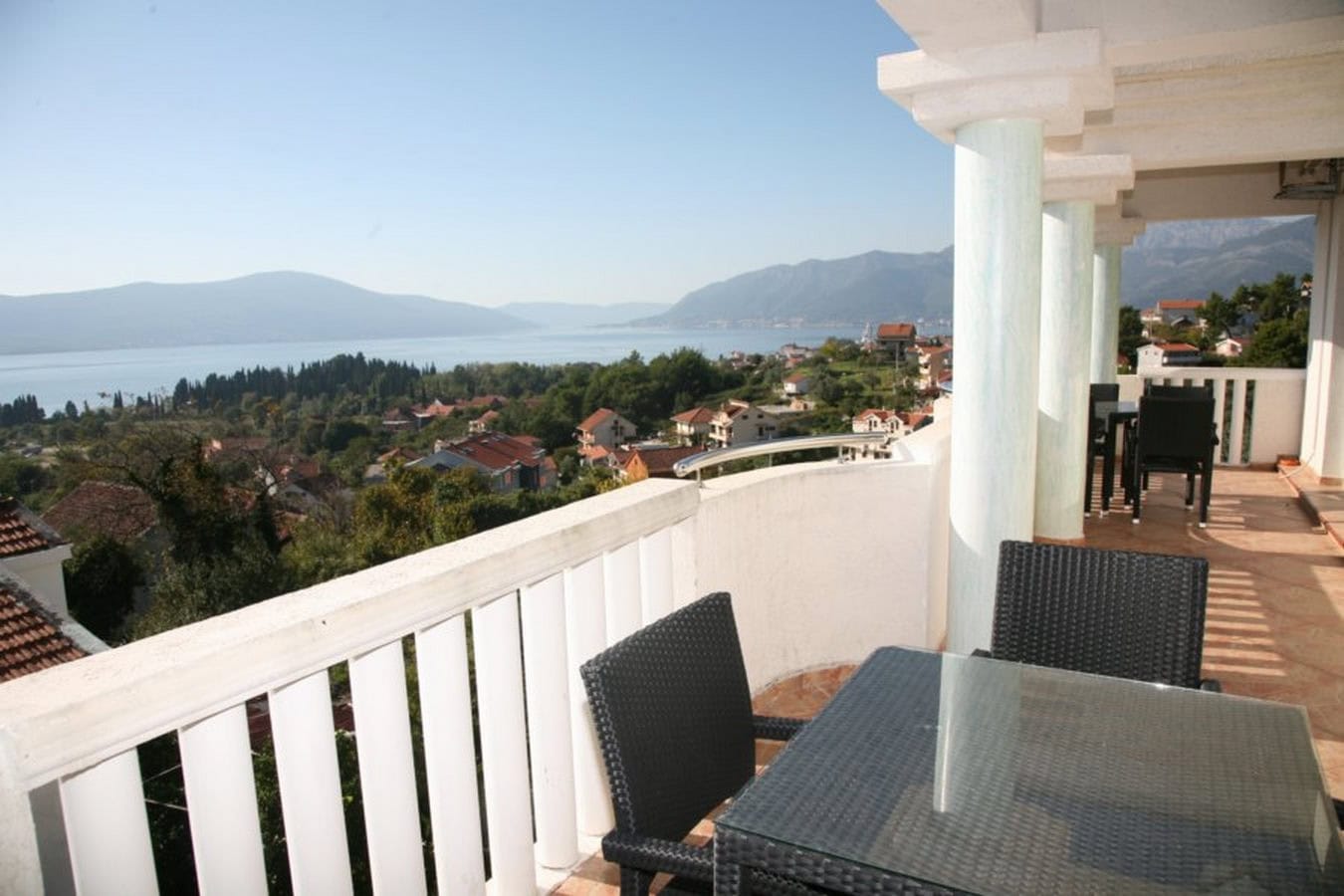 Villa terrace in Tivat, Montenegro: sea and mountain views, wicker furniture with a glass table, white columns.