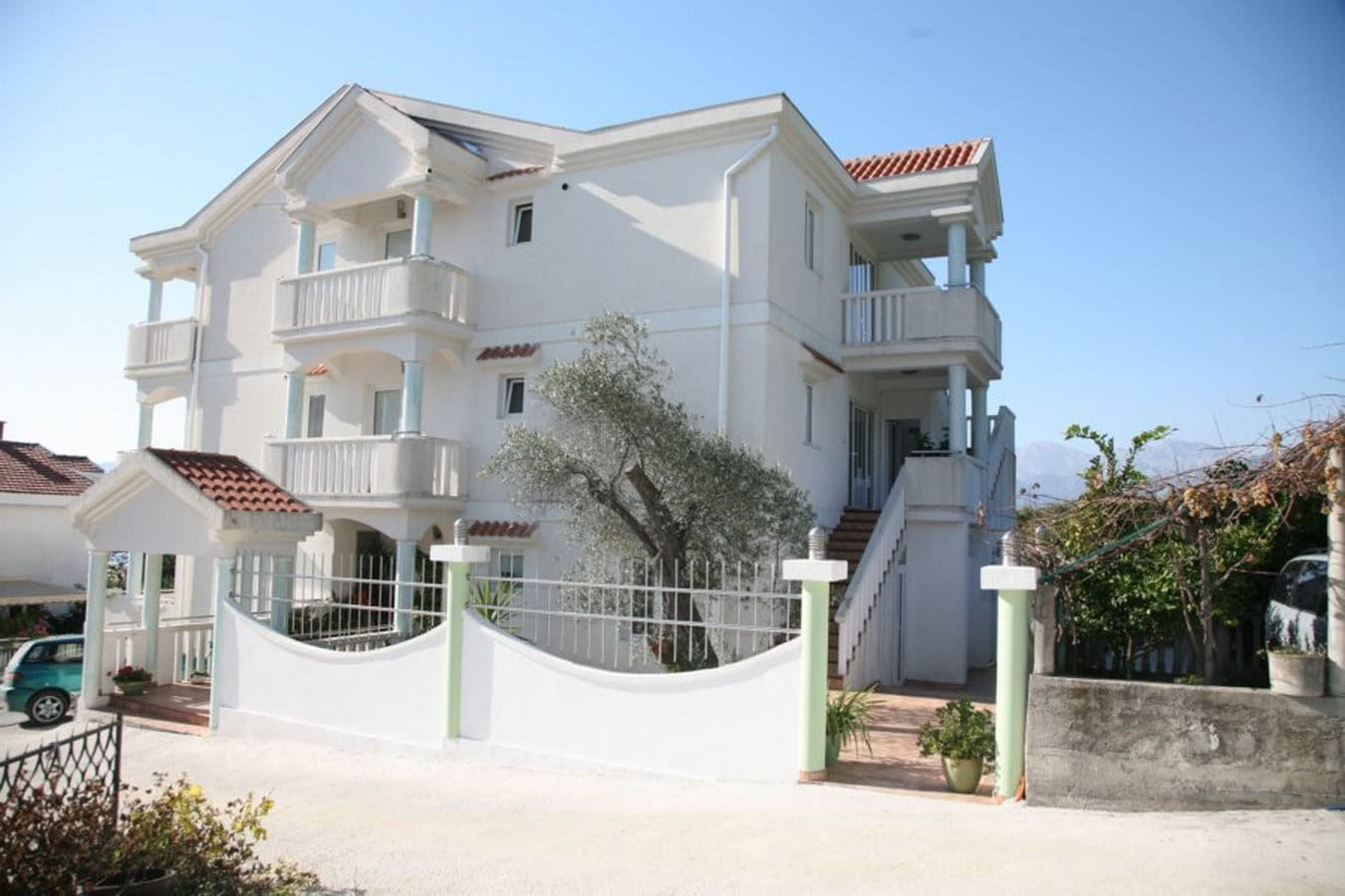 Three-story white villa with balconies and a fenced grounds in Tivat, Montenegro.