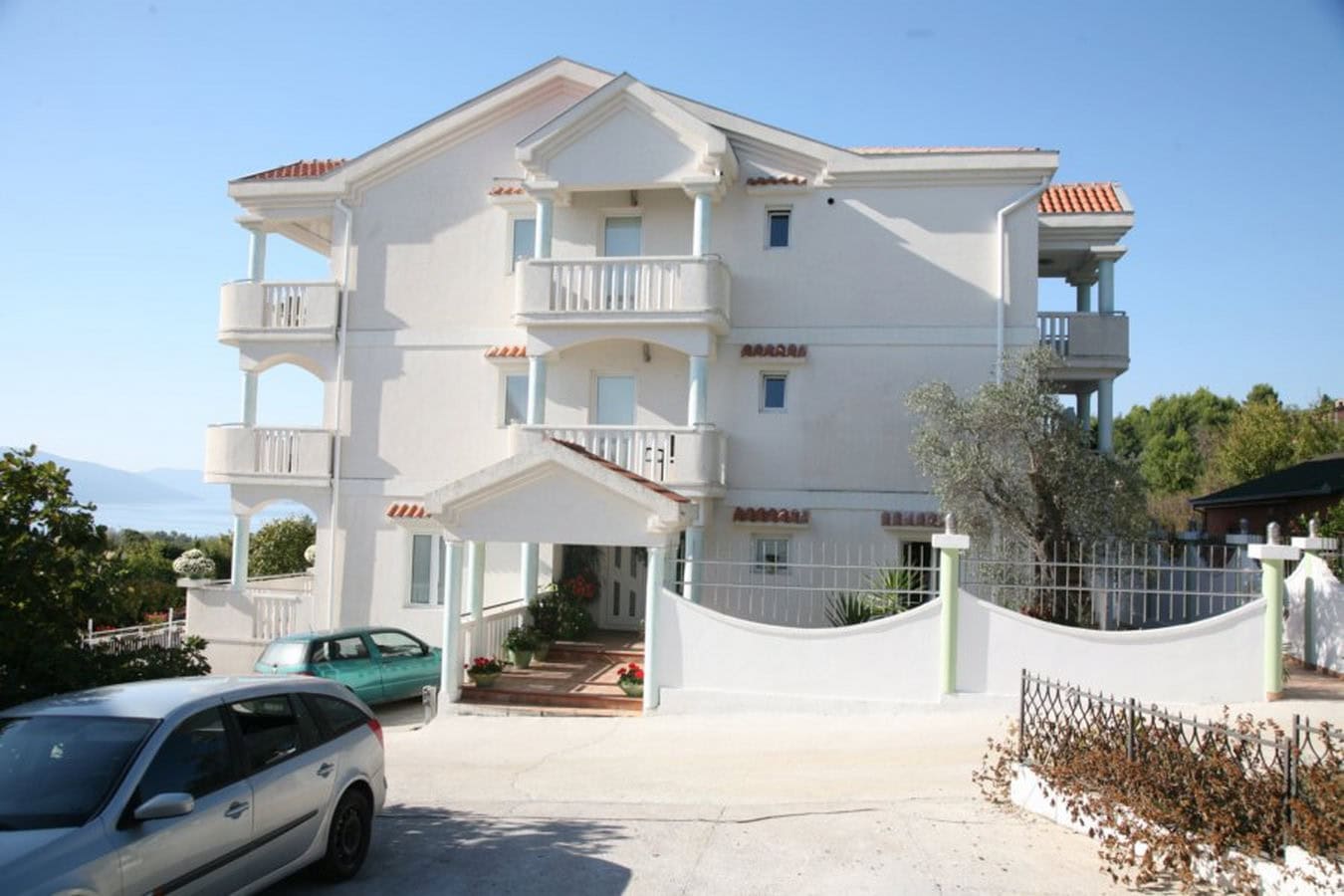 Three-story villa in Tivat, Montenegro: facade with balconies, parking, and sea view surrounded by greenery.