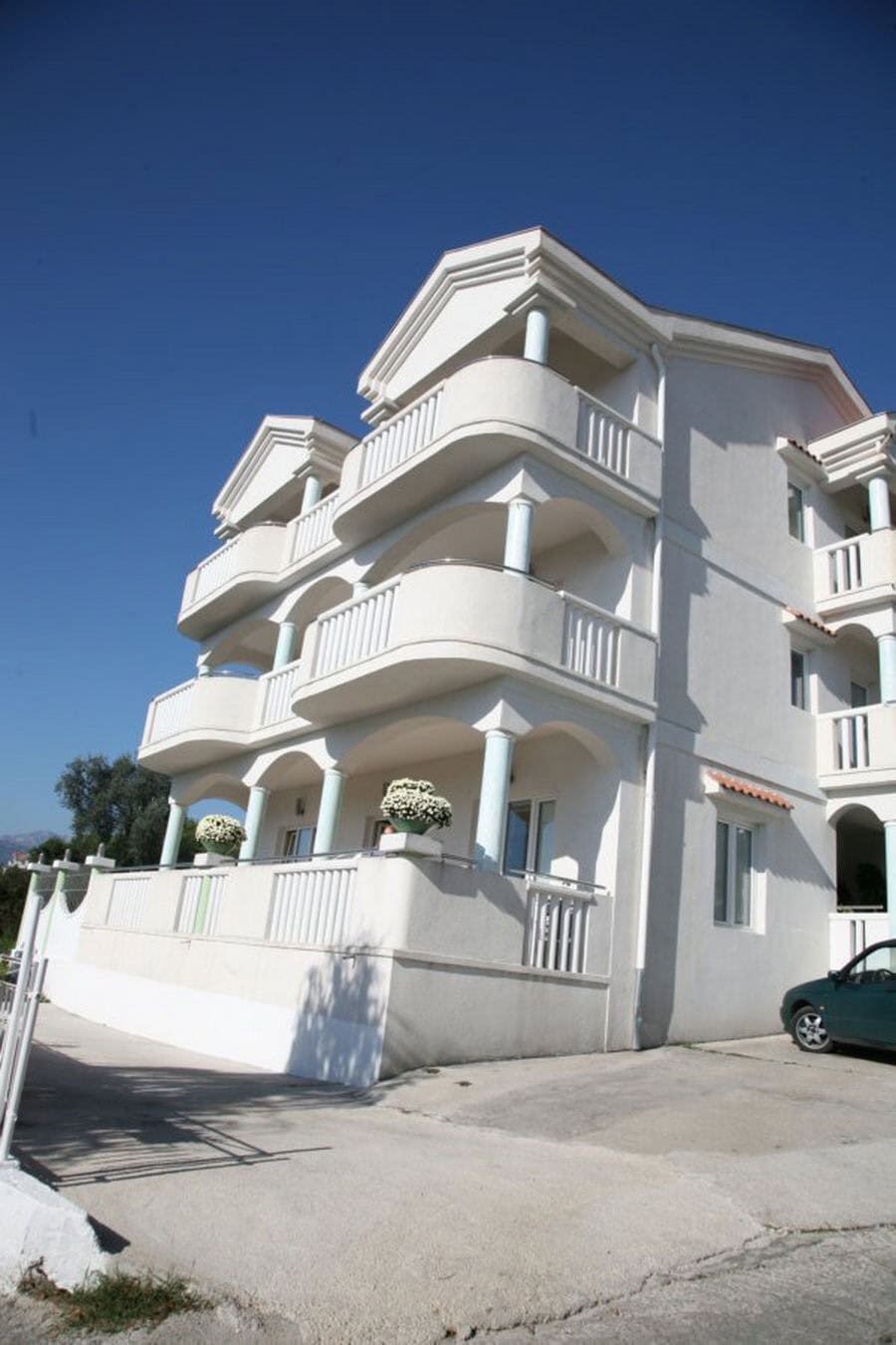 Three-story bright villa with terraces and columns in Tivat, Montenegro, front view of the building with parking.