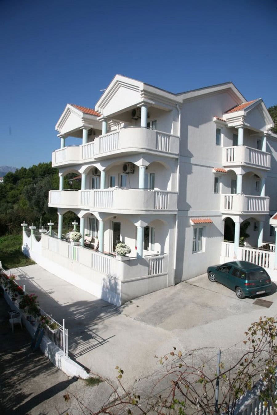 Three-story white villa in Tivat, Montenegro, with open terraces, columns, and parking by the house.