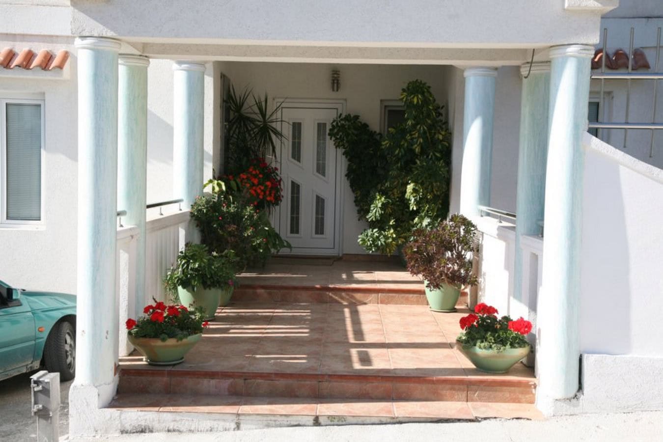 Entrance to a villa in Tivat, Montenegro: a porch with columns, terracotta tiles, and decorative potted plants.