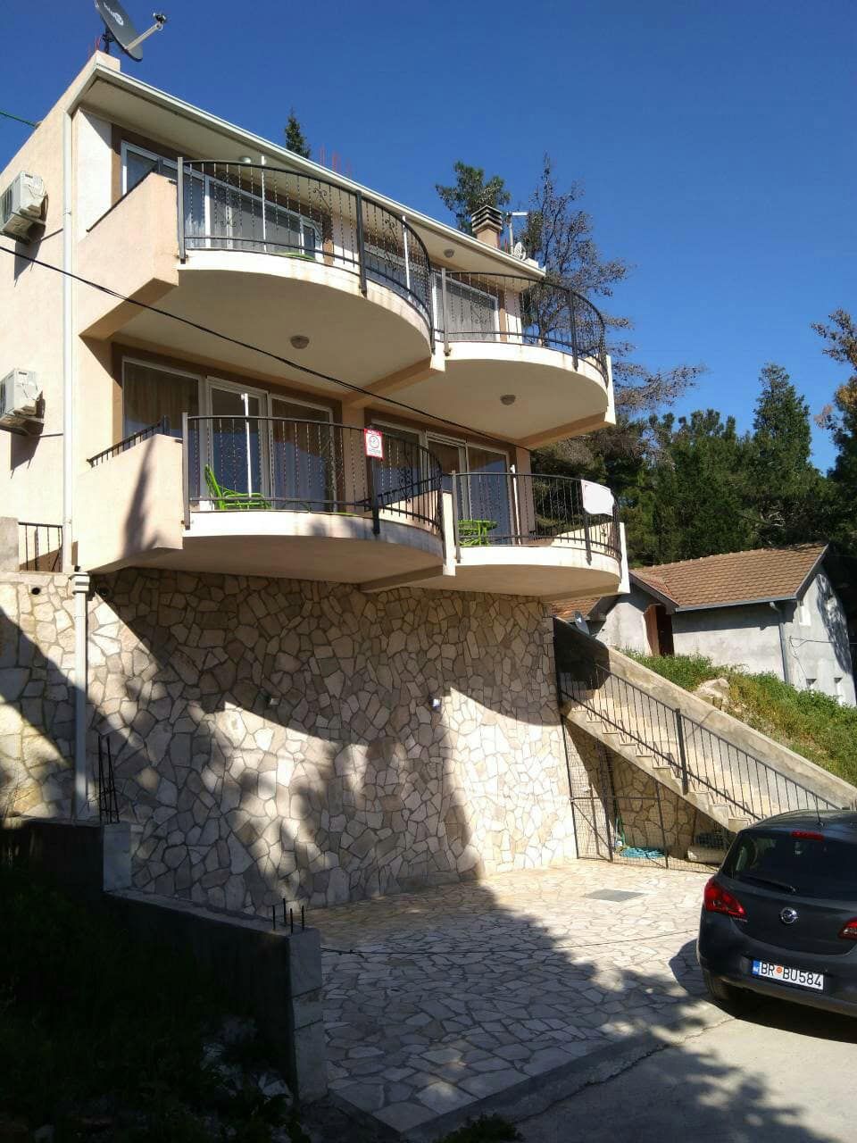 Two-story house in Shushan, Montenegro, with stone facade cladding, balconies, and private parking by the building.