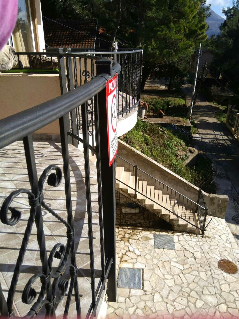 View from the balcony of a house in Shushan, Montenegro: wrought-iron railings, tiled floor, and stairs leading to the yard.