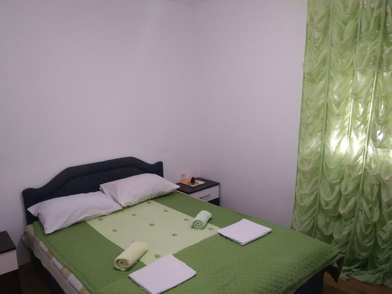 Cozy bedroom with a double bed in a house in Shushan, Montenegro: light finishes and green curtains.