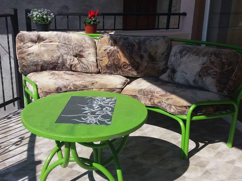 Cozy terrace with a green sofa and round table in a house, Shushan, Montenegro. Open balcony with tiles and flowers.